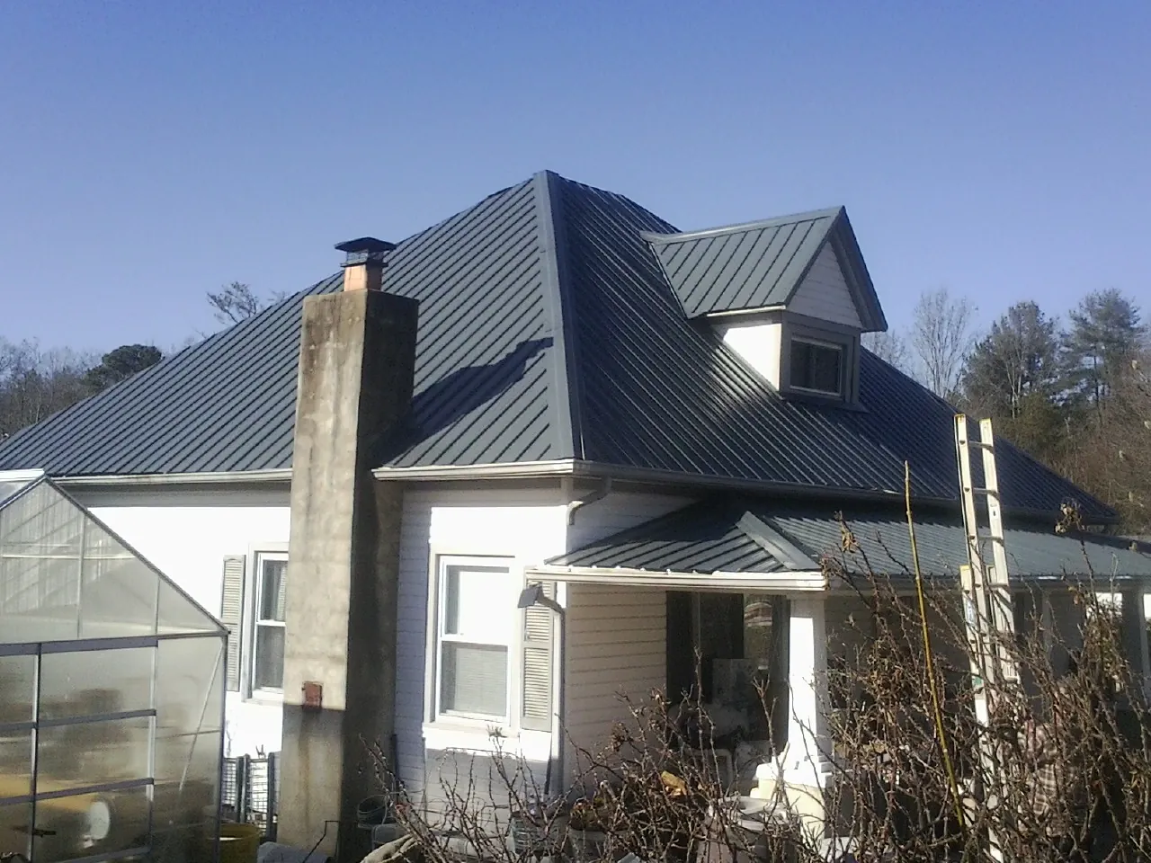Dark blue standing seam metal roof on a white farmhouse with dormer — Slate & Tile Roof Repair by Roofing Brothers in Idledale