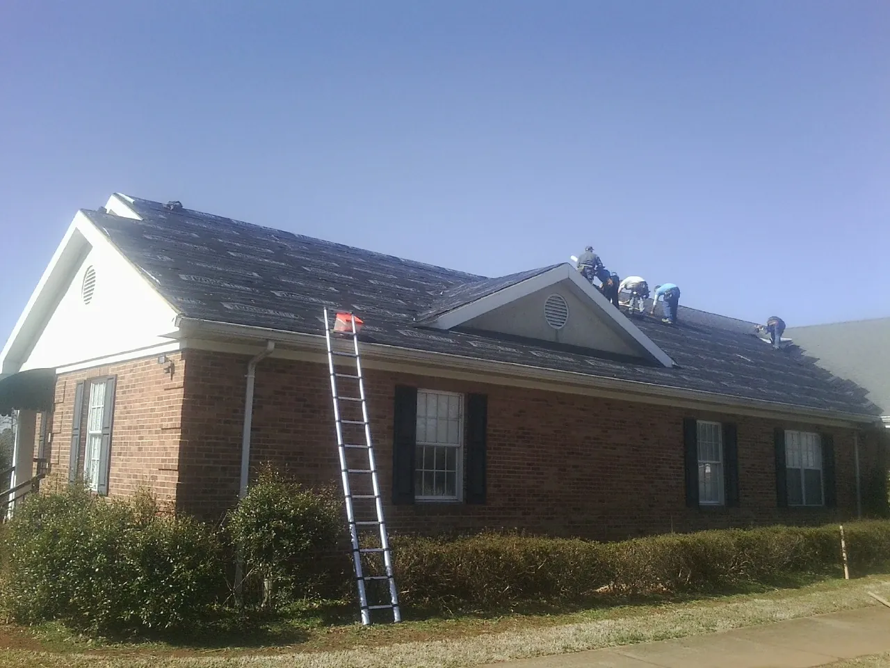 Crew tearing shingles off a brick ranch roof with a ladder set — Metal Roof Repair work by our crew in Idledale