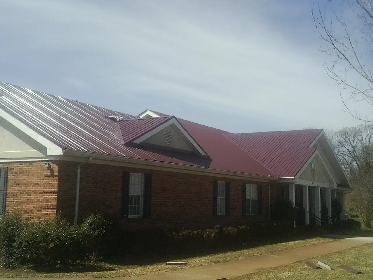 Red metal roof with gabled entries on a long brick building, from a Hail Damage Roof Repair job in Idledale