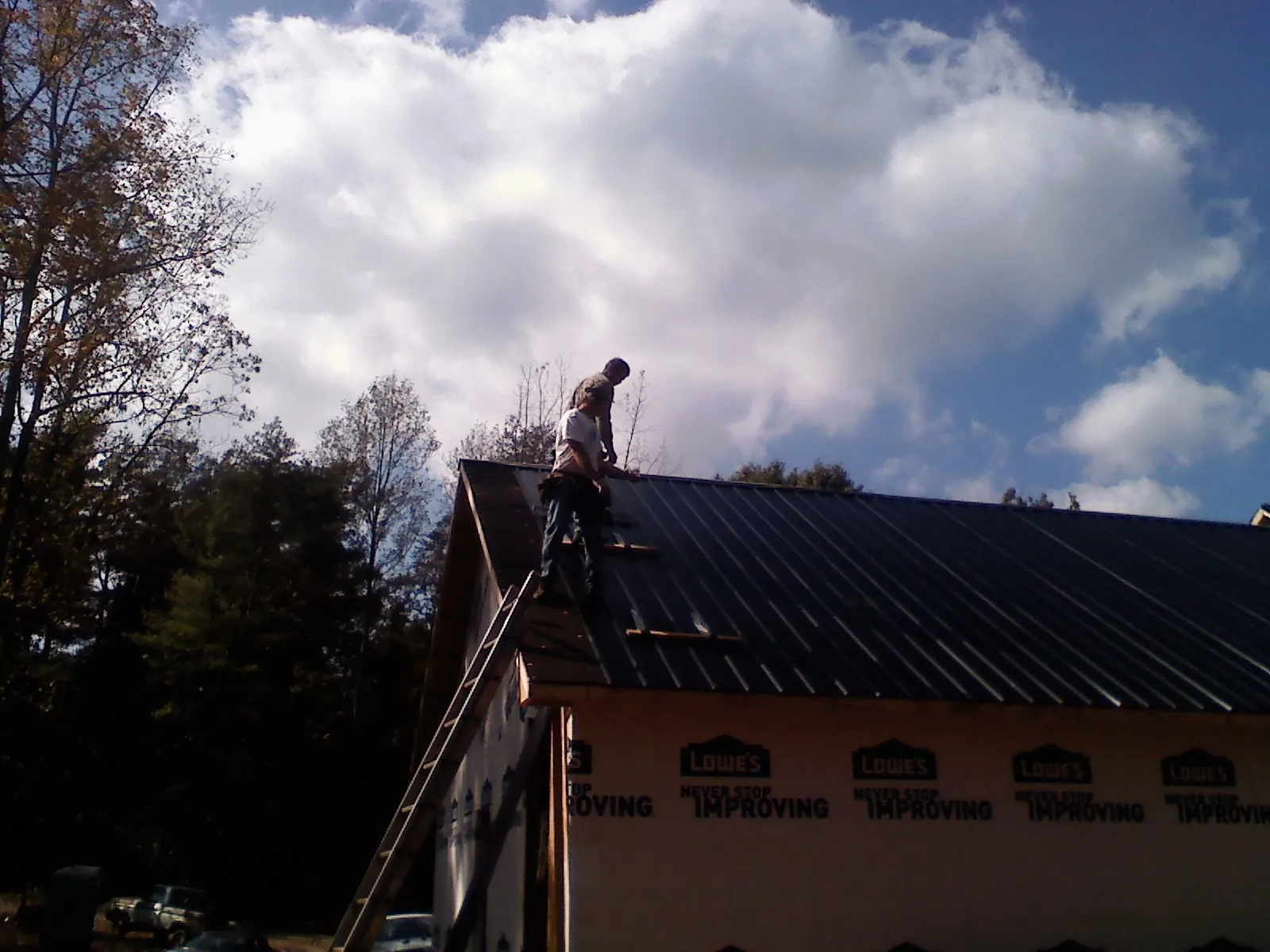 Roofer fastening dark metal panels high against a cloudy sky, from a Roof Inspection job in Idledale