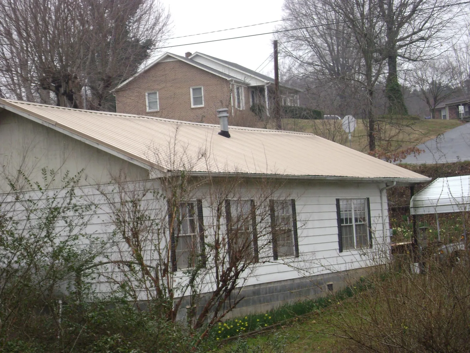 Tan metal roof on a white sided house set into a hillside — Commercial Roofing by Roofing Brothers in Idledale