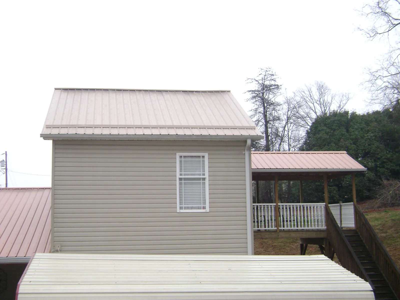 Tan metal roofs on a two story addition and attached porch, from a Roof Replacement job in Idledale